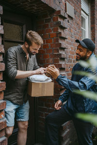 Mature man doing electronic signature while receiving parcel from delivery person standing at doorstep