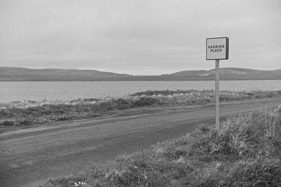 Road sign on field against sky