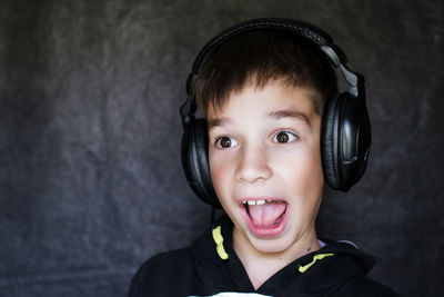 Close-up of surprised boy listening music against wall