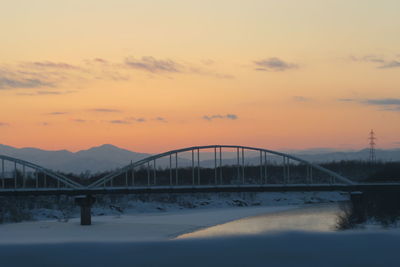 Bridge over snow covered mountains against sky during sunset