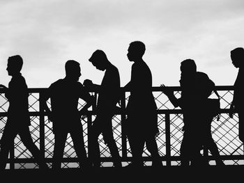 Silhouette men standing by railing against sky