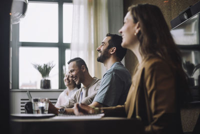 Happy businessmen sitting by colleagues at conference table in creative office