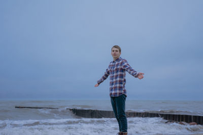 The guy spreads his hands from pleasure, on the seashore, in a plaid shirt