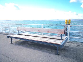 Empty bench by sea against sky