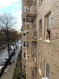 Woman looking out of window of apartment building on street in city during pandemic 