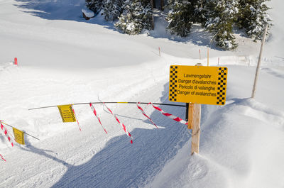 Yellow avalanche warning sign in snow covered landscape, grindelwald, switzerland