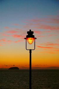 Silhouette lamp by sea against sky during sunset