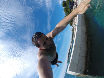 Low angle view of shirtless man jumping in river against sky on sunny day