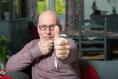 Portrait of bald mature man gesturing thumbs up on sofa at home