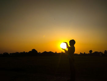 Silhouette man standing on field against sky during sunset