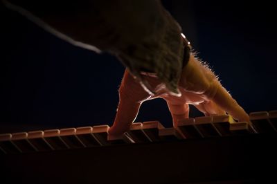 Cropped hand of man playing piano against black background