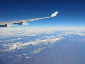 Aerial view of airplane wing over landscape against blue sky