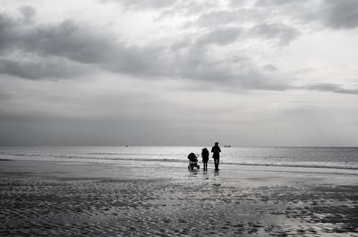 Silhouette people with baby carriage at beach against sky