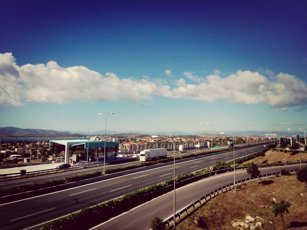 transportation, sky, road, blue, built structure, road marking, landscape, architecture, cloud - sky, cloud, mountain, railroad track, the way forward, high angle view, building exterior, city, highway, street, outdoors, horizon over land