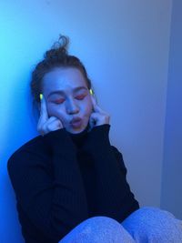 Portrait of woman sitting against blue wall