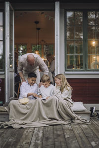 Man talking to children using digital pc while sitting on porch