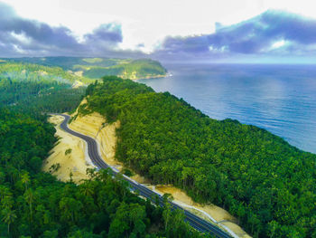 A curvy coastal road snaking along a bright blue ocean. lush green vegetation