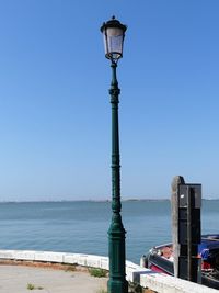 Street light by sea against clear blue sky