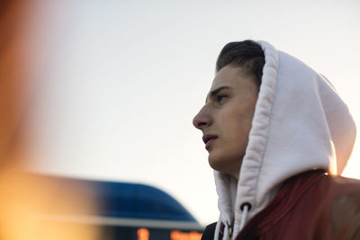 Low angle view of thoughtful teenager wearing hooded shirt standing against clear sky
