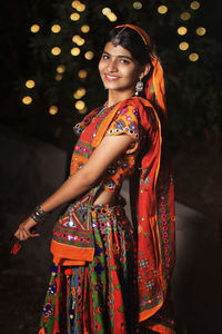 Portrait of young woman standing against illuminated christmas tree