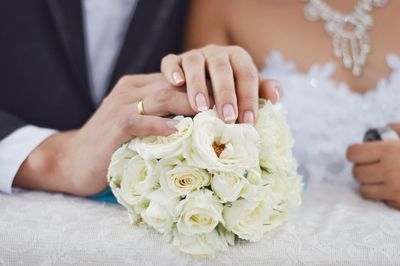 Cropped image of bride and groom touching rose bouquet