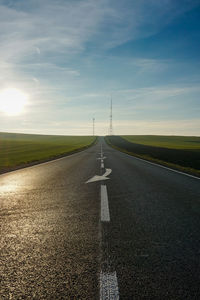 Empty road amidst field against sky