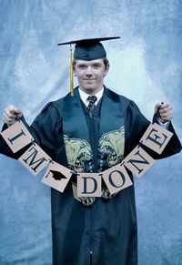 Portrait of teenage boy wearing graduation gown while holding text