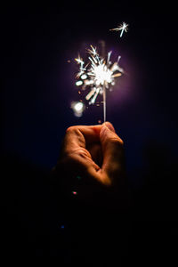 Cropped hand holding lit sparkler at night