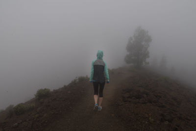 Rear view of woman walking on hill against sky during foggy weather