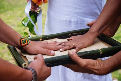 High angle view of bride and bridegroom positioning hands on bamboo tray during wedding