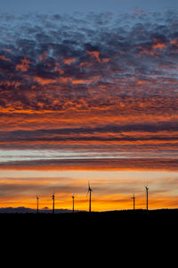 Silhouette of wind turbines on field during sunset