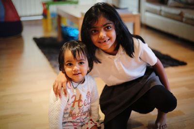 Cute sisters sitting on hardwood floor at home