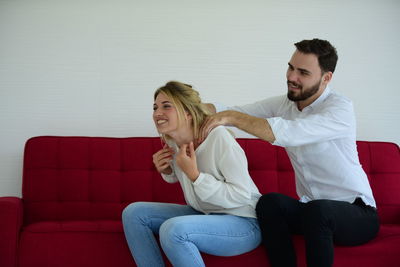 Young man massaging woman while sitting on sofa at home