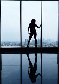 Silhouette man standing by window against sky