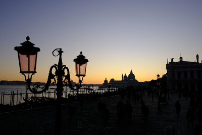 Silhouette people on street against sky during sunset