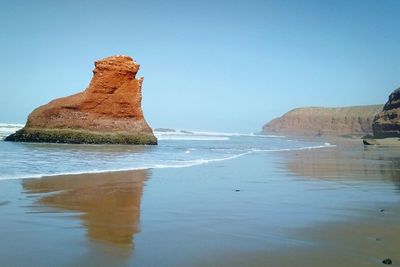 Rock formation on beach against clear blue sky