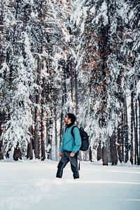 Young man walking on snow covered land against trees