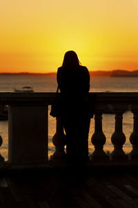 Silhouette woman looking at sea against sky during sunset