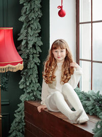 Happy young girl sitting by the window and christmas tree