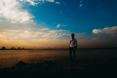 Silhouette man standing at beach against sky during sunset