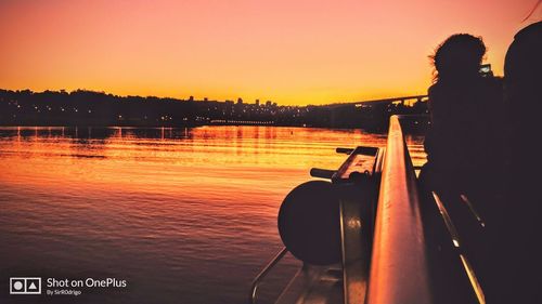 Silhouette man on boat in lake against orange sky