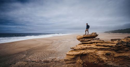 Man standing on rock at beach against sky