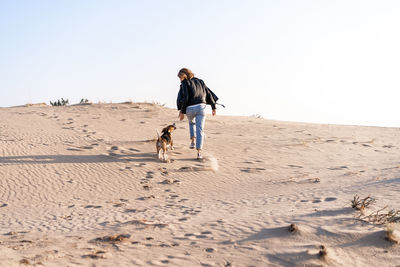 Rear view of woman with dog walking at beach