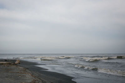 Waves reaching at beach against sky