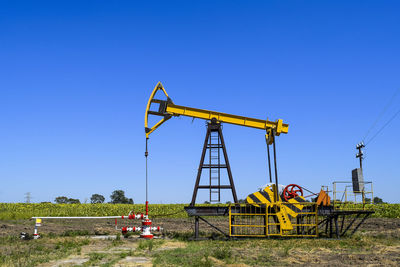 Oil drill on field against clear blue sky