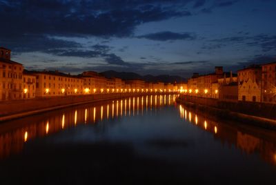 Illuminated city by river against sky at night