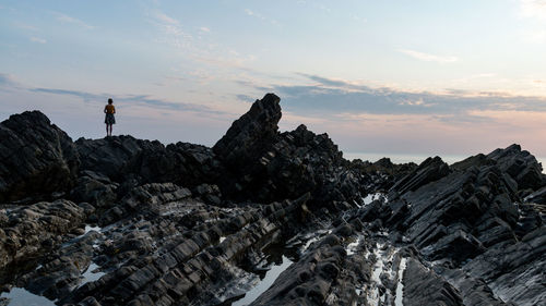 Women standing on rock against sky during sunset