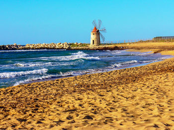 Lighthouse on beach against clear blue sky