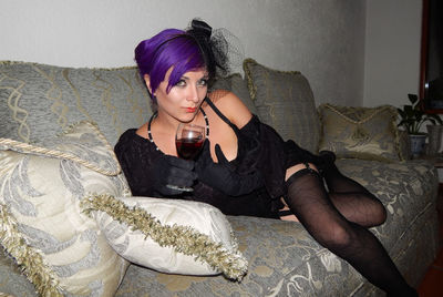 Portrait of seductive woman having wine while relaxing on sofa at home