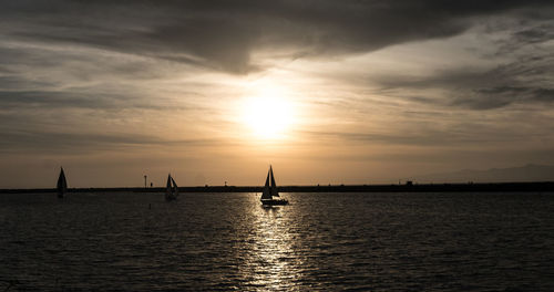 Silhouette sailboat in sea against sky during sunset